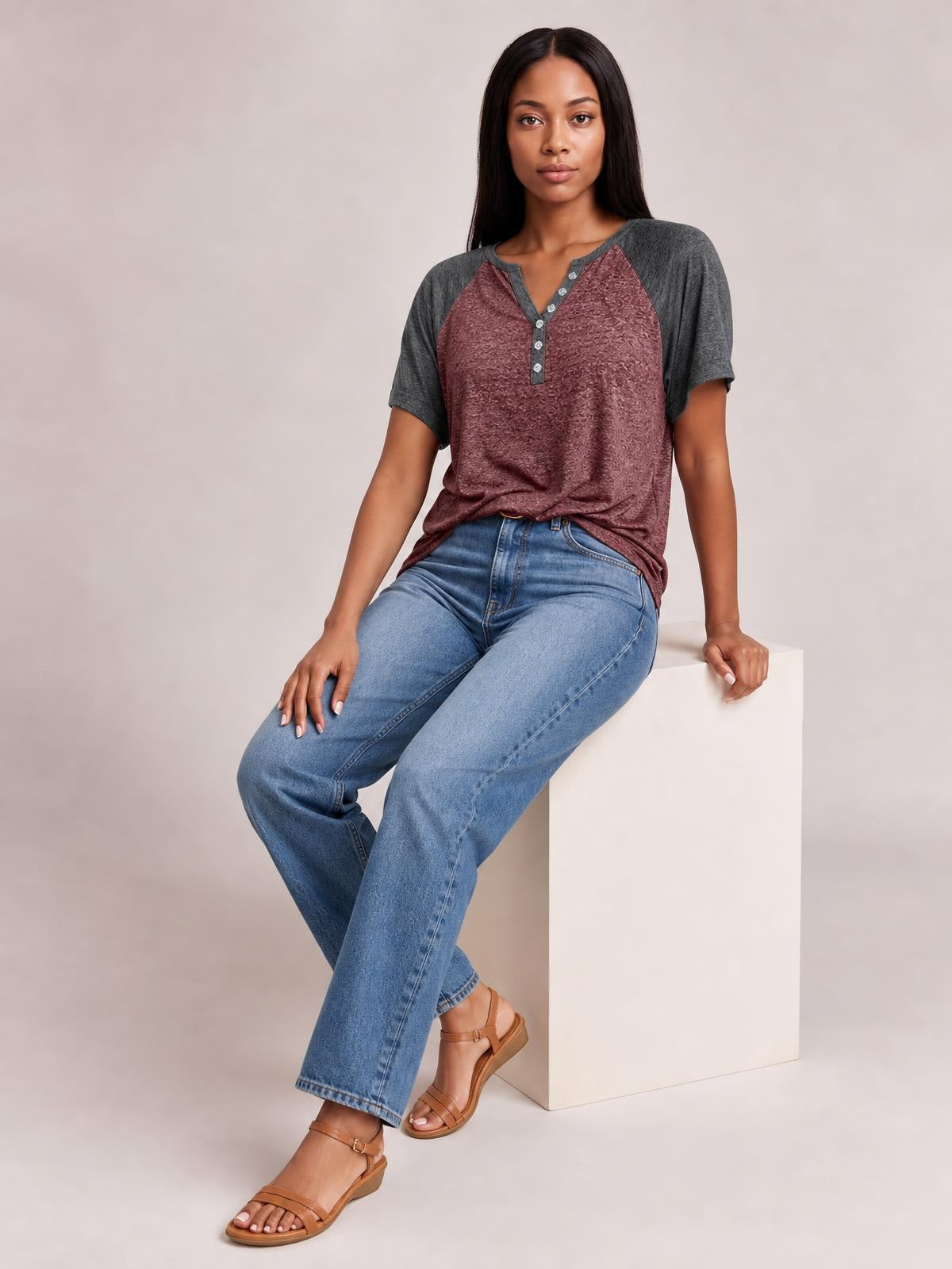A seated model wears a burgundy and gray contrast notched short sleeve T-shirt with a relaxed silhouette and decorative button placket.