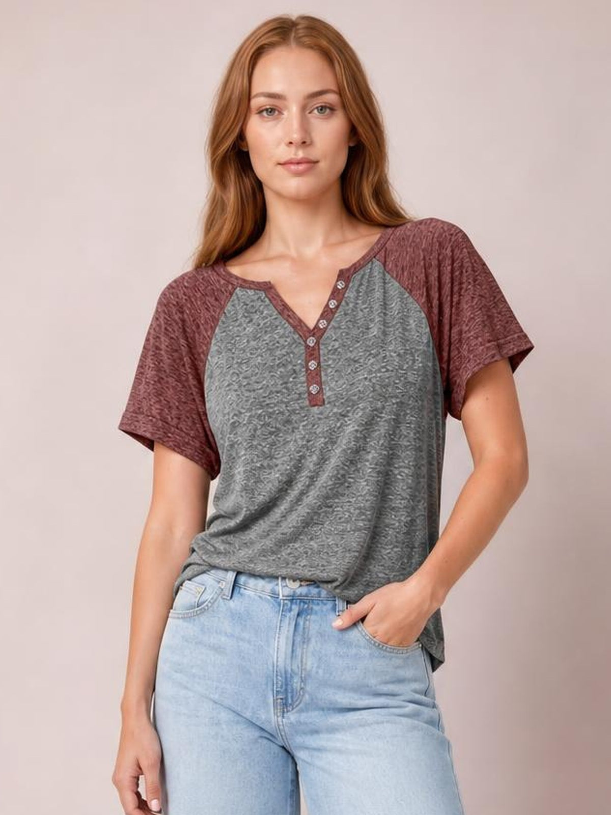 Model wearing a relaxed gray contrast short sleeve T-shirt with burgundy sleeves, a notched neckline, decorative button placket, and a loose silhouette.