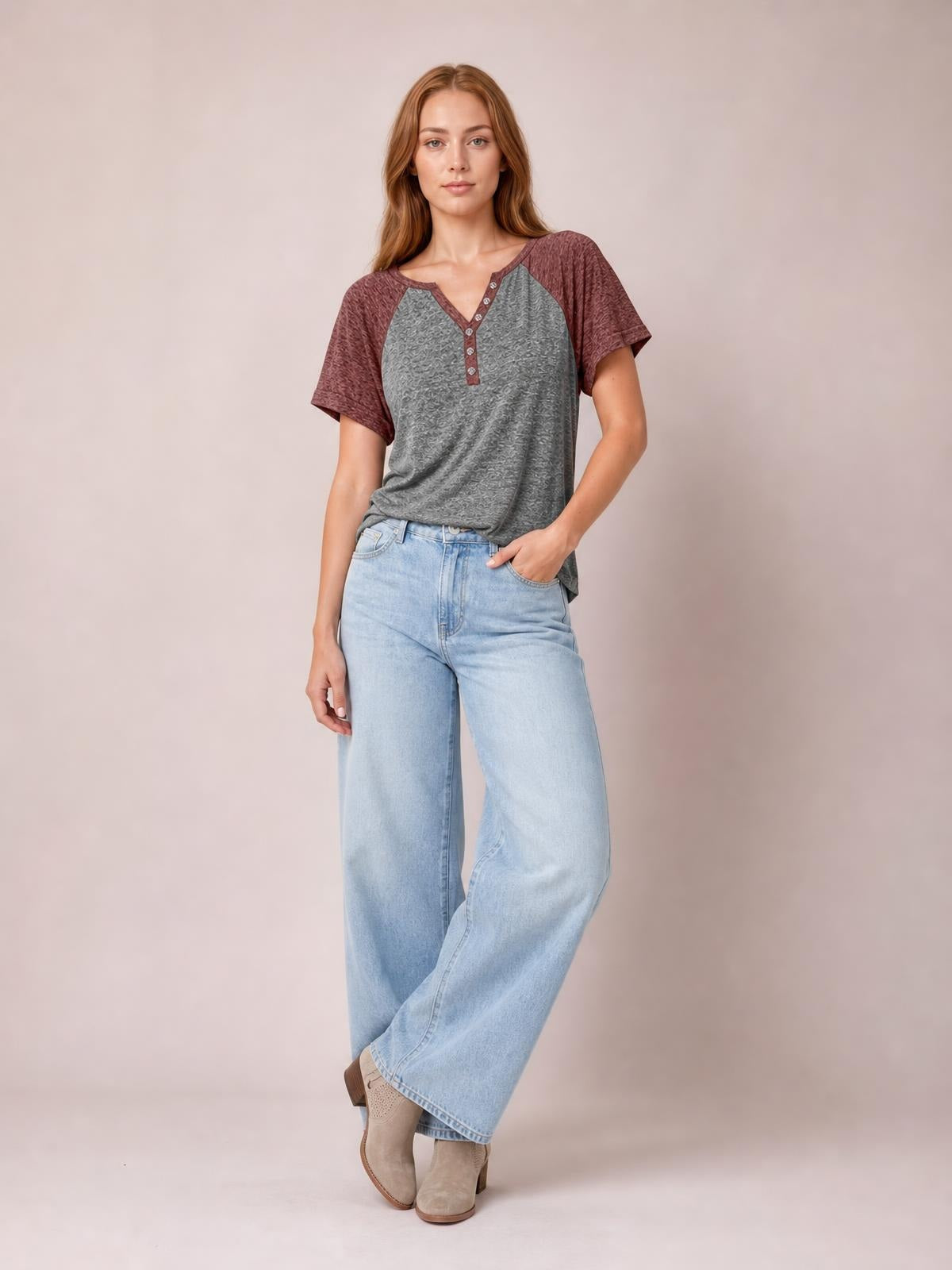 Model poses in a relaxed contrast short sleeve T-shirt with a gray body, burgundy sleeves, notched neckline, and decorative button placket.