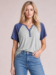 Model poses in a gray and navy contrast short sleeve T-shirt with a notched neckline, decorative button placket, and relaxed silhouette.