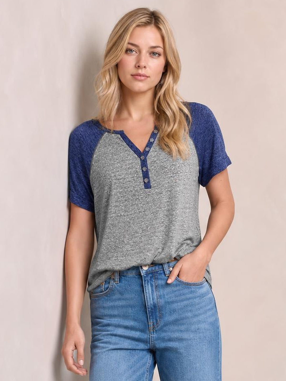Model poses in a gray contrast notched short sleeve T-shirt with navy raglan sleeves, a buttoned neckline, and a relaxed silhouette.