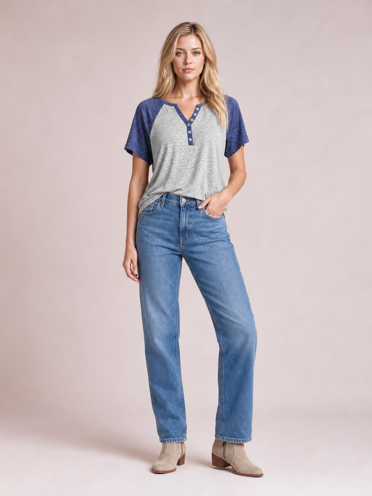 A woman stands in a relaxed pose wearing a gray contrast notched short sleeve T-shirt with blue raglan sleeves, a button placket, and an easy silhouette.