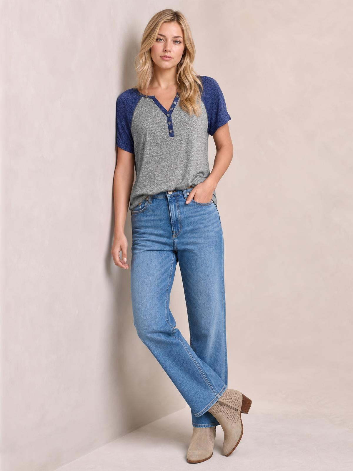 Model wears a gray contrast notched short sleeve T-shirt with blue raglan sleeves, button placket, and relaxed silhouette, posing with one hand in her pocket.