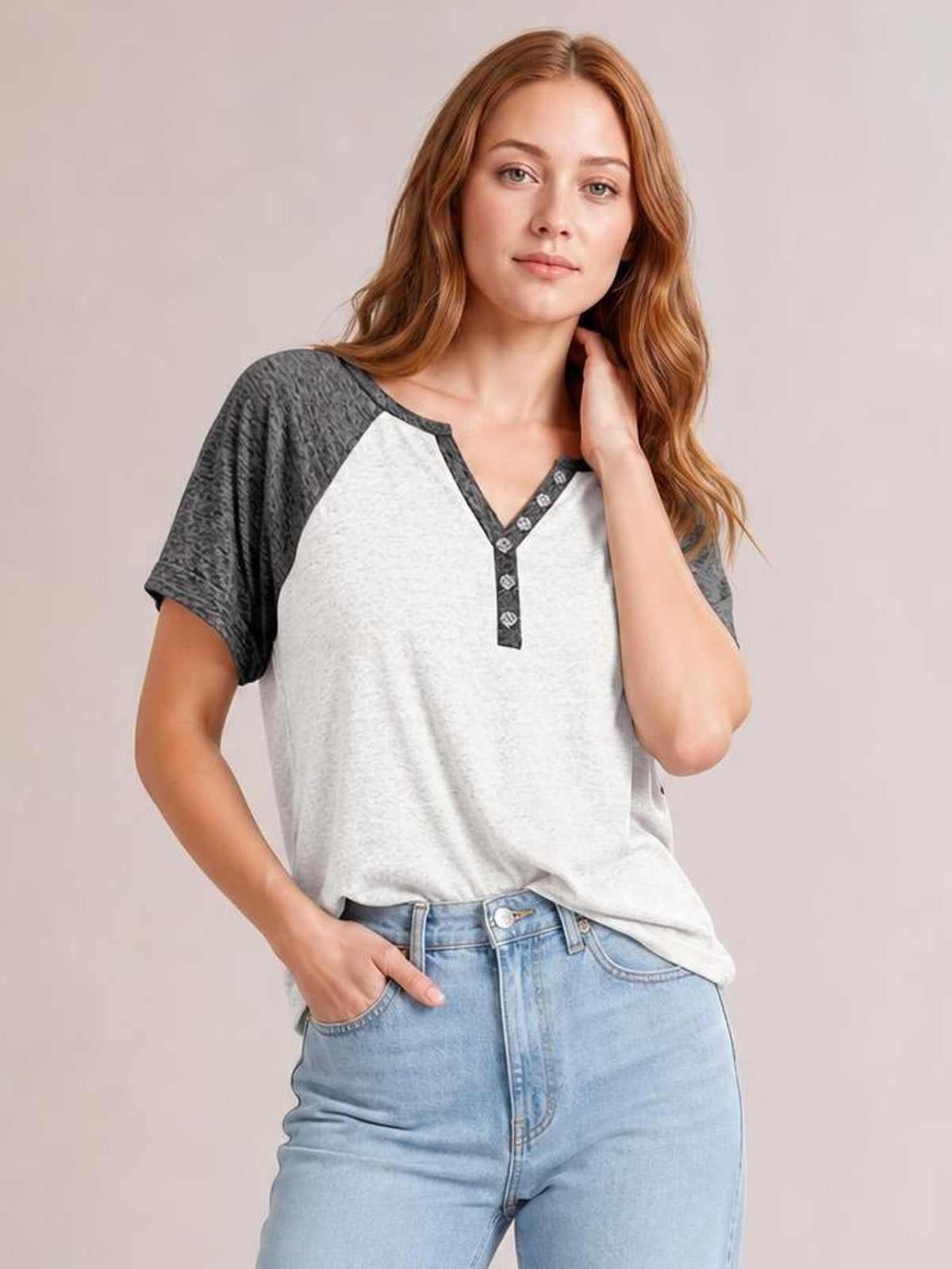 A model poses in a relaxed contrast notched short sleeve T-shirt with a light gray body, dark raglan sleeves, decorative buttons, and a loose silhouette.