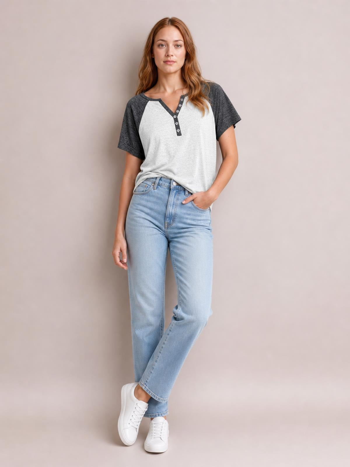 A model wears a light gray contrast notched short sleeve T-shirt with charcoal raglan sleeves, a decorative button placket, and a relaxed silhouette, posing with one hand in her pocket.