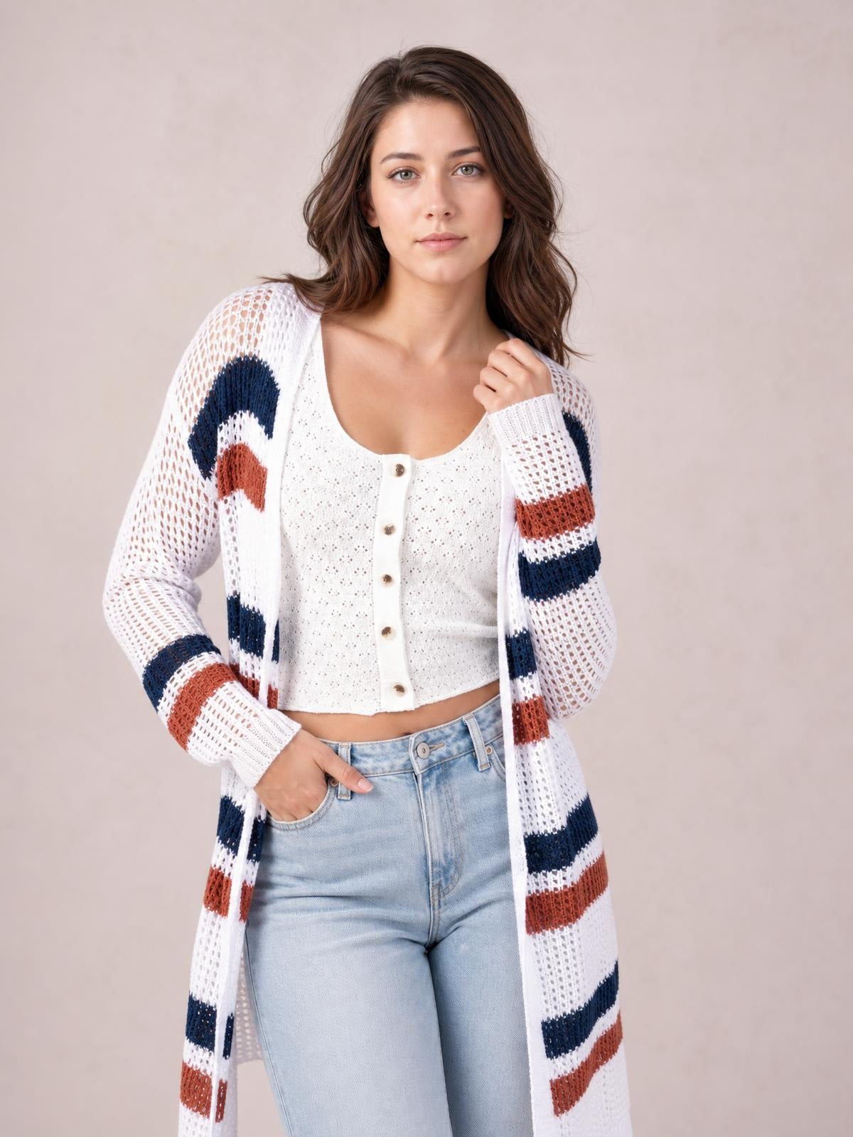 Model poses in a white contrast openwork cardigan with navy and rust stripes, long sleeves, open front, and a longline silhouette, holding the collar with one hand.