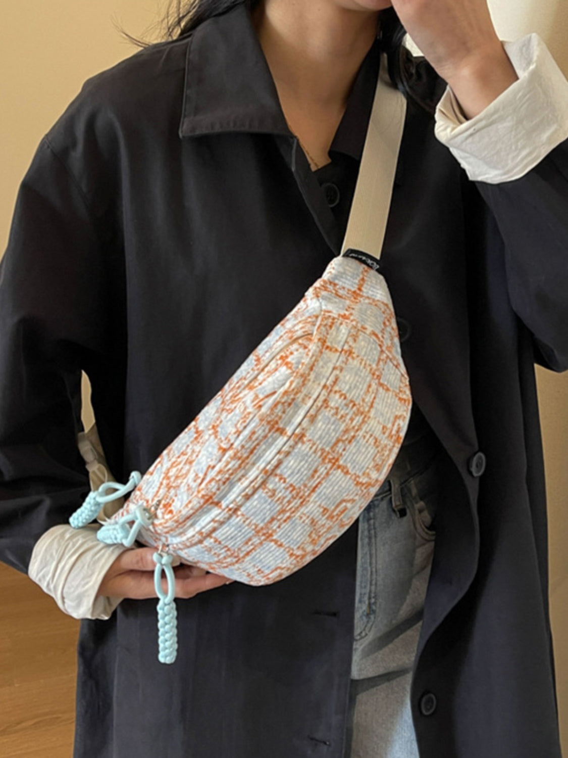A model holds a softly curved medium polyester crossbody bag in contrasting gray and rust plaid, with a long strap and playful cord accents.