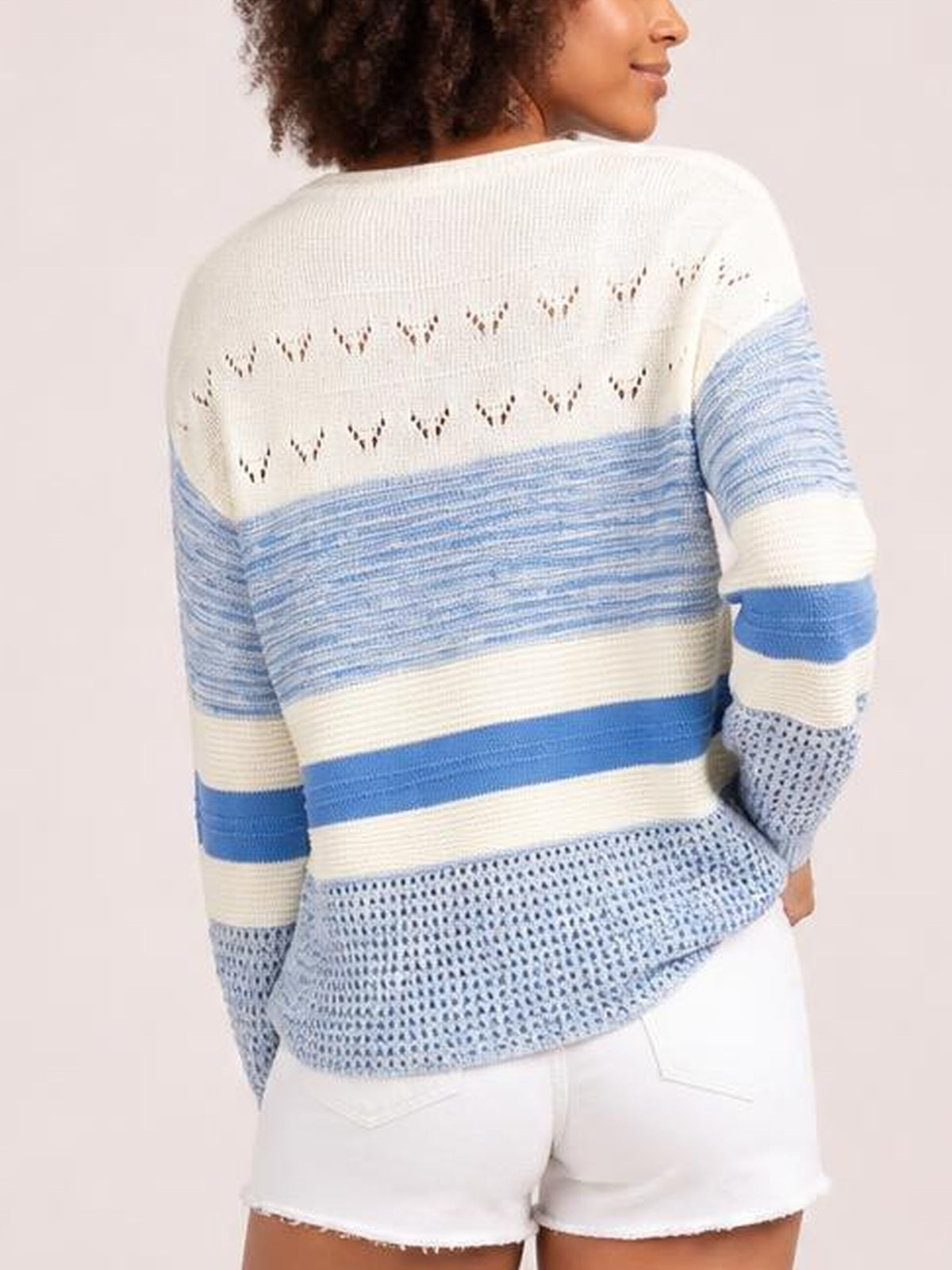 Model shown from behind wearing a blue and ivory contrast round-neck long-sleeve sweater with striped knit panels, openwork detailing, and a relaxed silhouette.