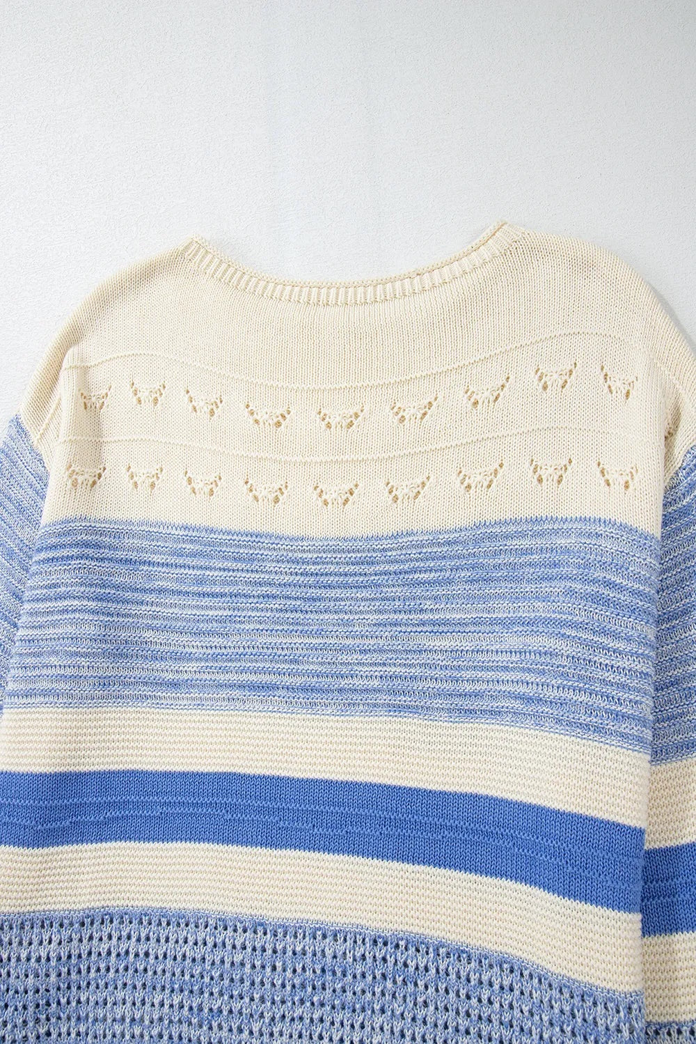 Close-up of a cream and blue contrast round neck sweater with long sleeves, horizontal stripes, open-knit detailing, and a relaxed silhouette.