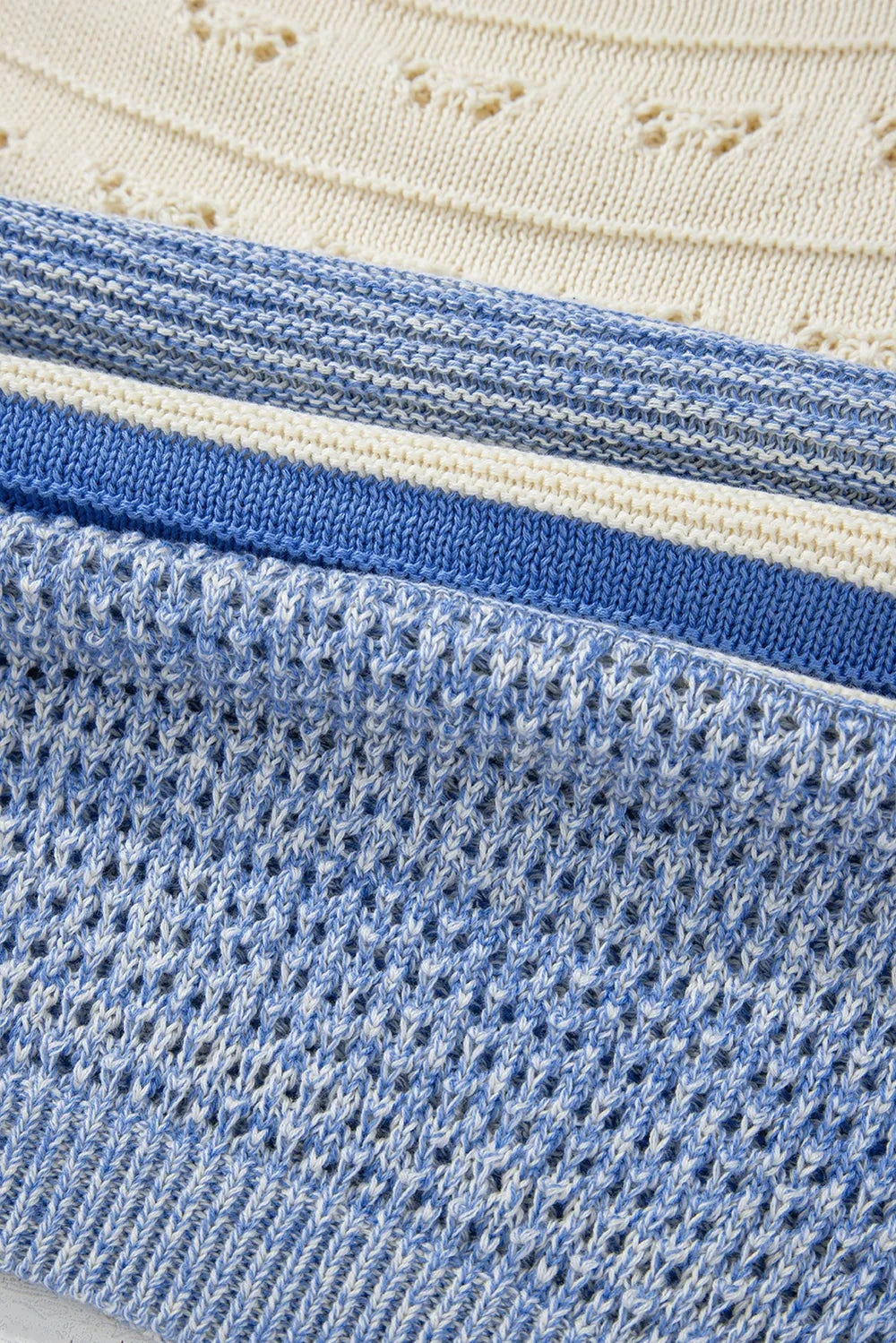 Close-up of a blue and white contrast knit sweater showing a textured stitch pattern and ribbed hem construction.