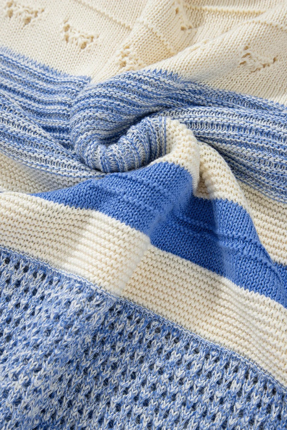 Close-up of a blue and cream contrast knit sweater showing textured stitching, ribbed construction, and varied horizontal color blocking.