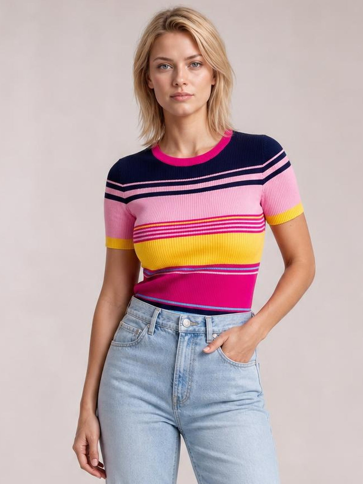 Model standing with one hand in her jeans pocket, wearing a fitted multicolor contrast round-neck short-sleeve sweater with horizontal striped sections.