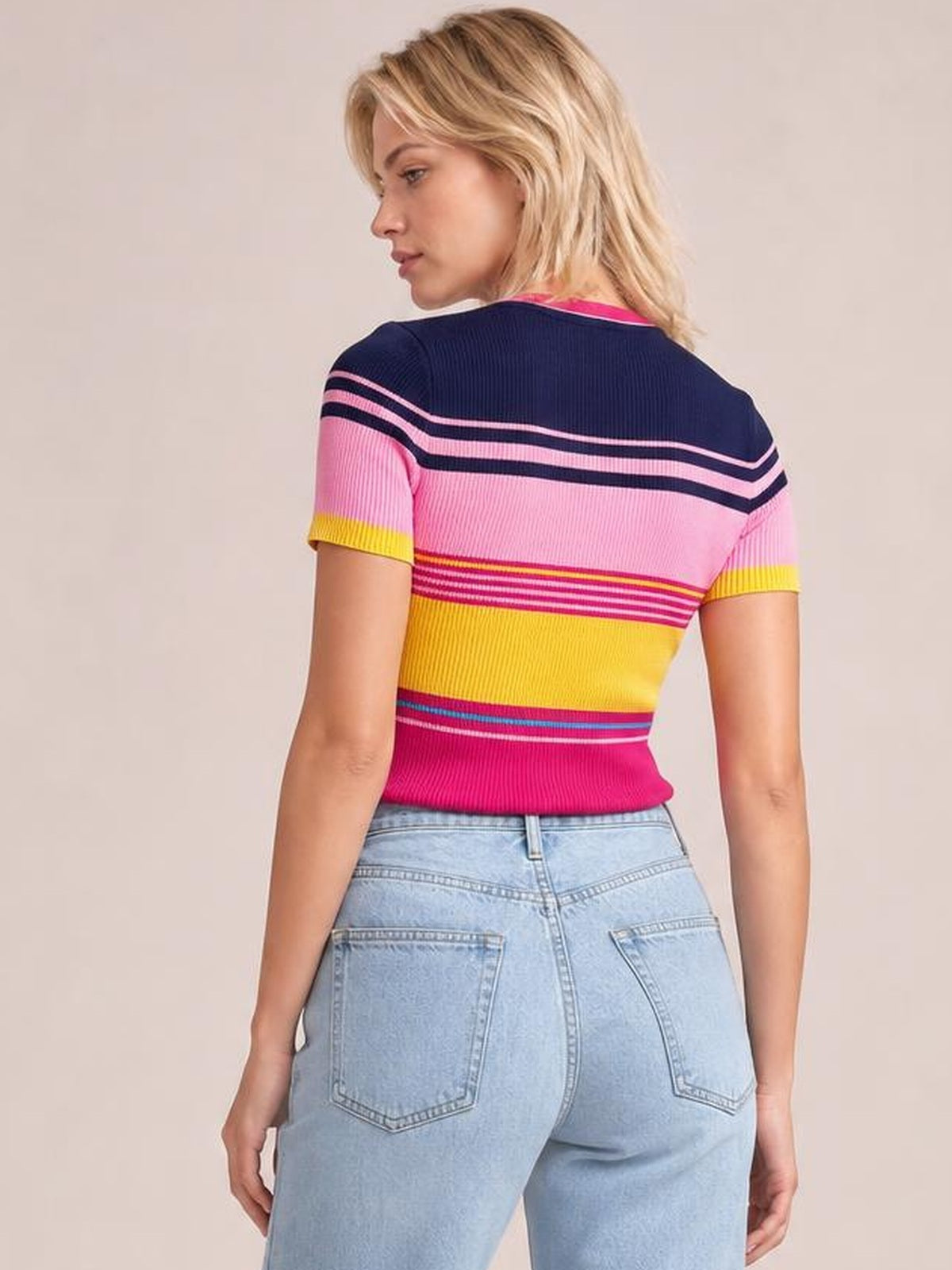 Model shown from behind wearing a fitted short-sleeve sweater with a round neck, multicolor contrast stripes, ribbed construction, and a pink, yellow, and navy palette.