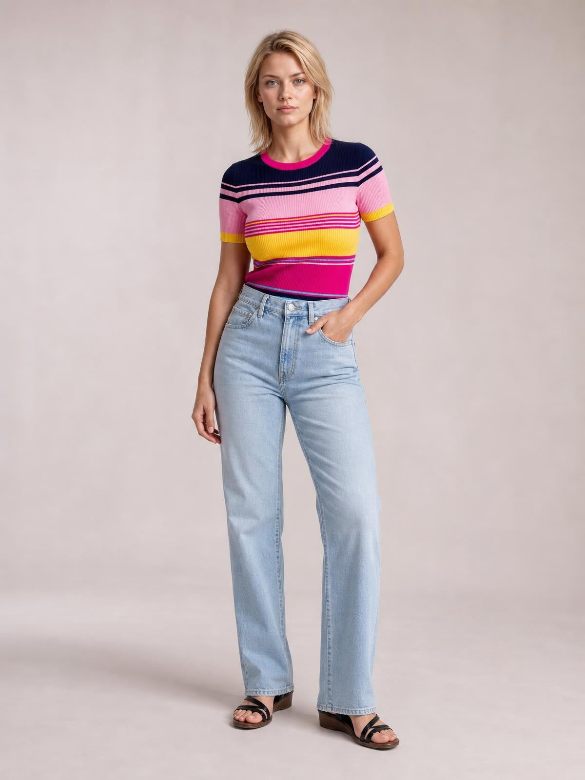 Model wears a fitted contrast round neck short sleeve sweater with colorful horizontal stripes and ribbed trim, standing with one hand in her jeans pocket.