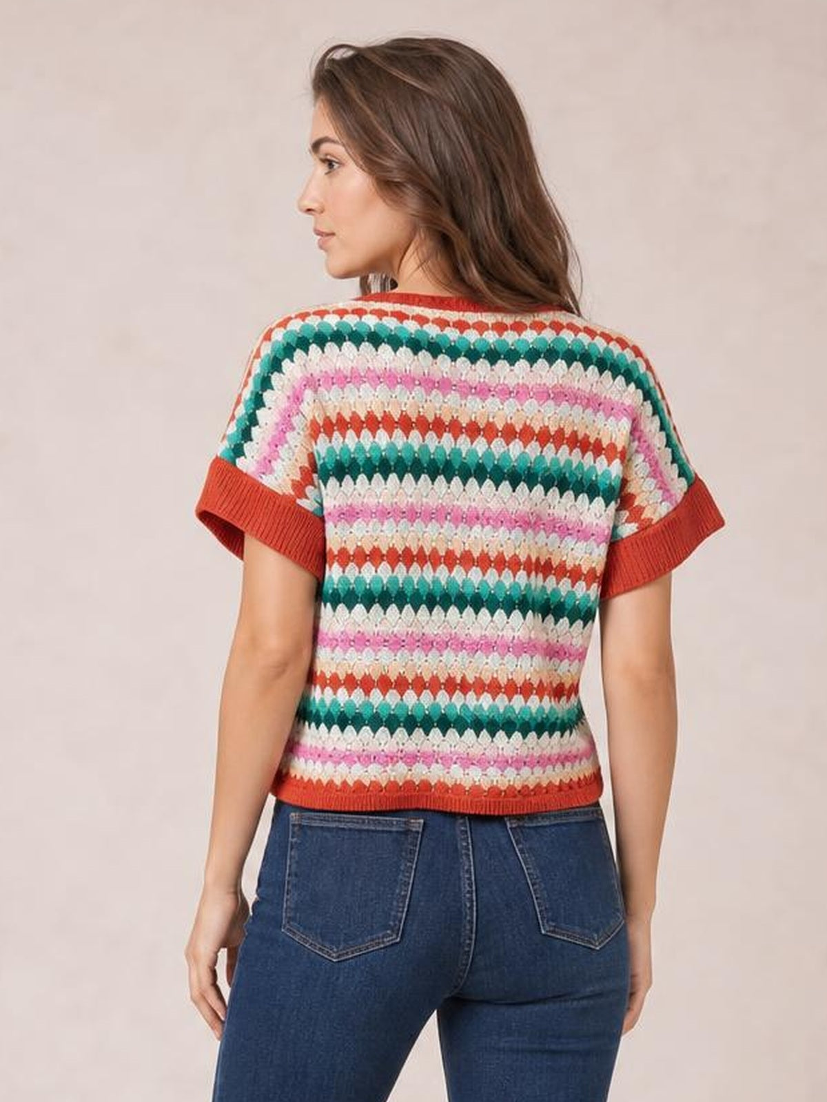 Model shown from behind wearing a multicolor striped contrast sweater with a round neck, short sleeves, red ribbed trim, and a relaxed silhouette.