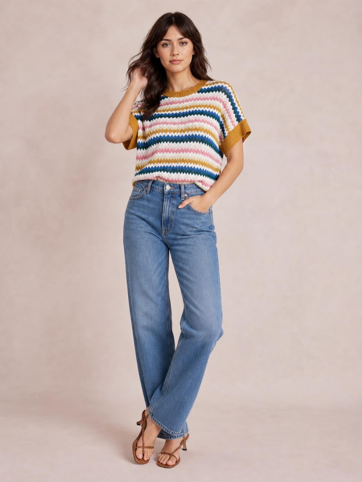 A model poses with one hand in her jeans pocket, wearing a relaxed multicolor contrast round-neck short-sleeve sweater with zigzag knit stripes and ribbed trim.