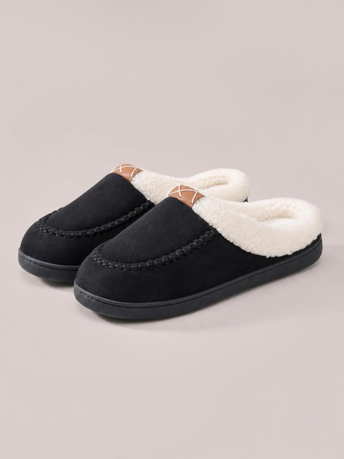 Pair of black round-toe flat slippers with contrast cream fluff lining, moccasin-style stitched uppers, brown accent tabs, and sturdy black soles.