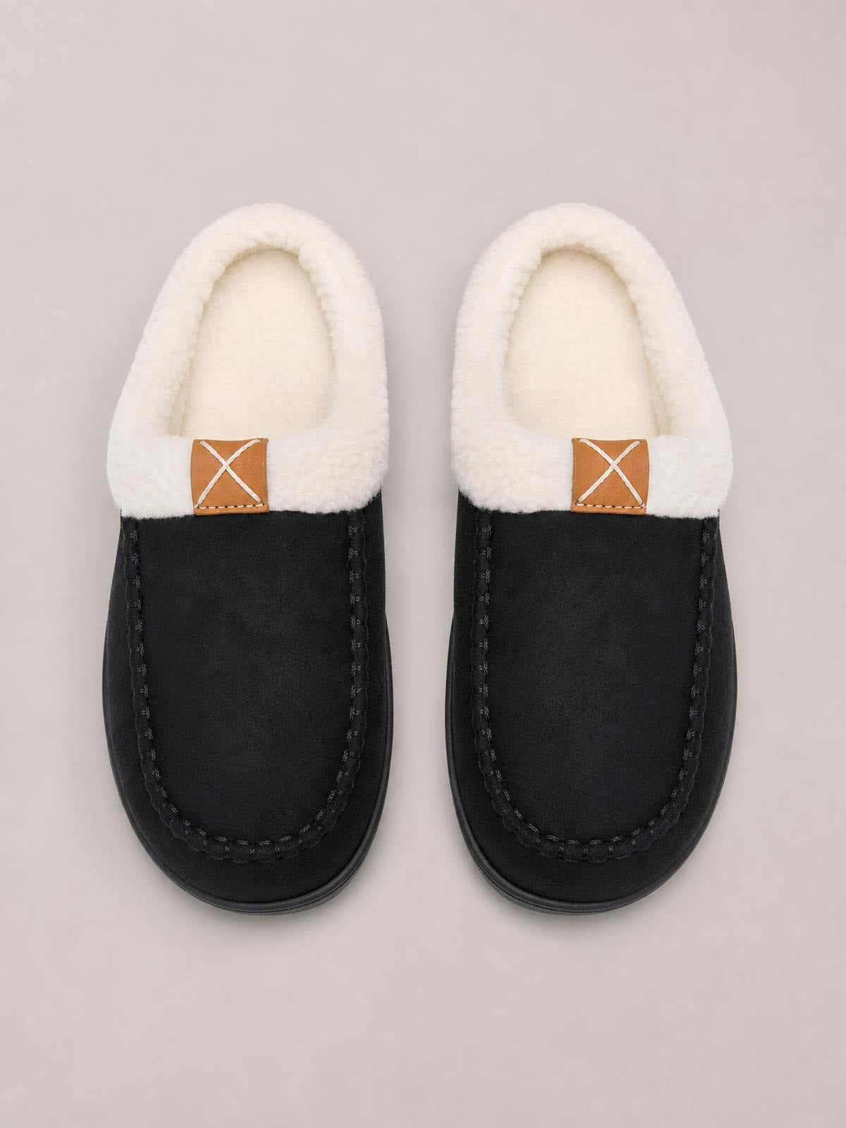 Black and cream contrast round toe flat slippers feature plush fluff lining, moccasin-style stitching, and brown crossed-detail tabs.
