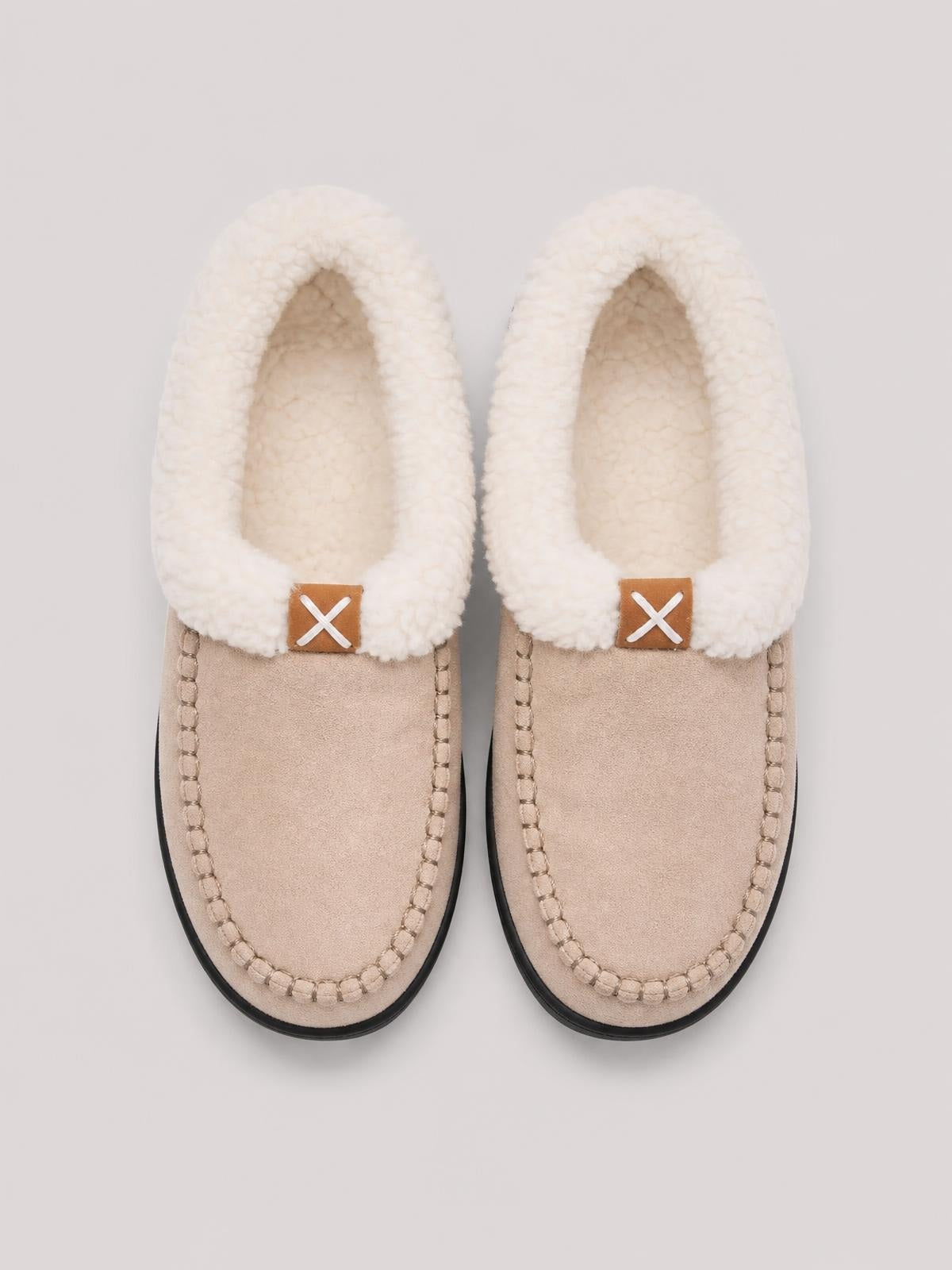 Beige contrast round-toe flat slippers feature plush cream fluff lining, moccasin-style stitching, brown tabs with white X accents, and black soles.