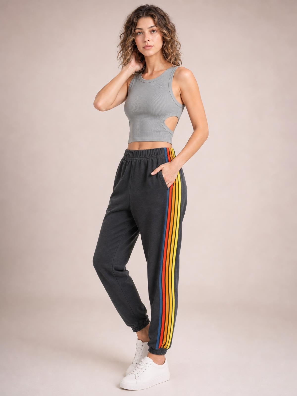 Model poses with one hand in the pocket wearing black active pants with a gathered elastic waist, tapered jogger silhouette, and colorful contrast side stripes.