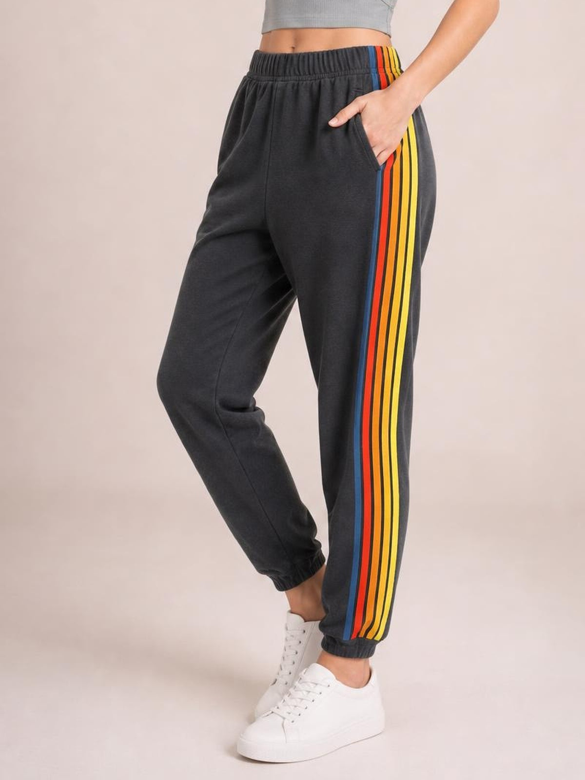 Model poses in dark jogger-style active pants with an elastic waist, tapered cuffs, side pockets, and bold multicolor contrast stripes.