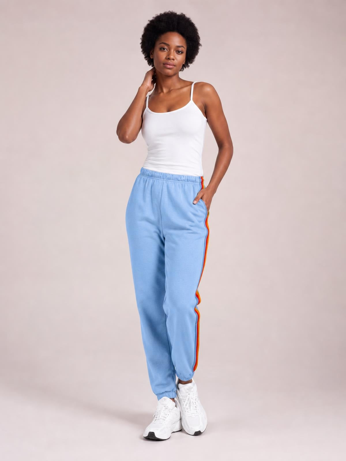 Model poses in light blue active pants with an elastic waist, contrast red and yellow side stripes, relaxed straight-leg silhouette, and cuffed ankles.