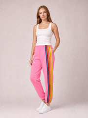 Model poses with one hand in the pocket, wearing pink active pants with a contrast multicolor striped leg, elastic waist, relaxed jogger fit, and cuffed ankles.