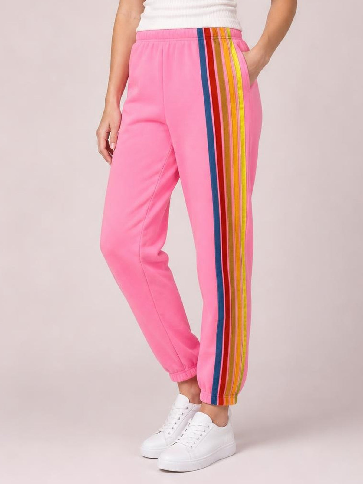 Model poses in pink active pants with an elastic waist, multicolor contrast side stripes, tapered legs, and gathered ankle cuffs.