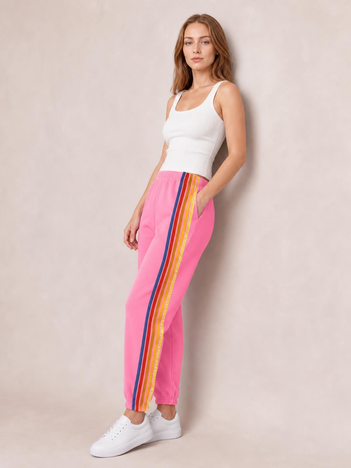 Model poses in pink active pants with a striped side panel, elastic waist, tapered legs, and cuffed hems, styled with a white tank top.