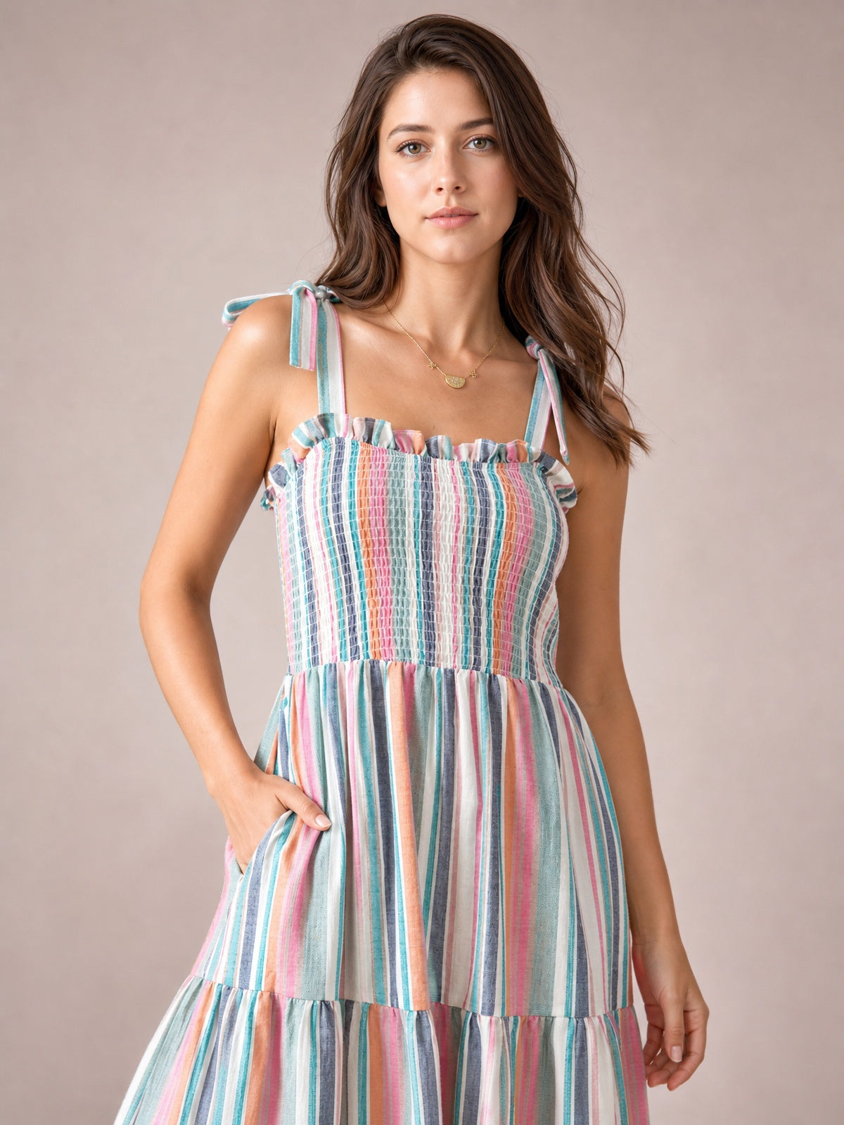Model poses with one hand in a pocket, wearing a colorful contrast striped square-neck cami dress with a smocked bodice, tied straps, frill trim, and tiered skirt.