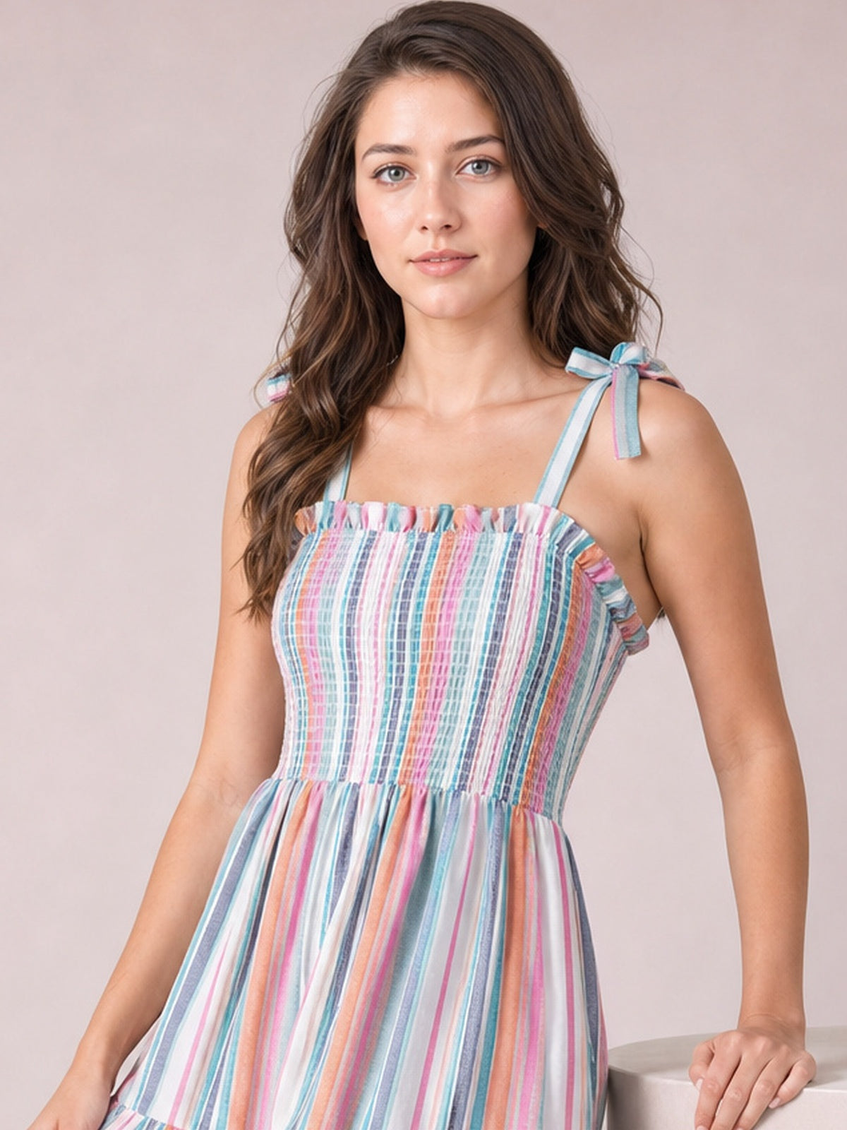 Model poses with one hand resting beside her in a colorful vertical-striped cami dress featuring a square neckline, tied straps, ruffle trim, smocked bodice, and tiered skirt.