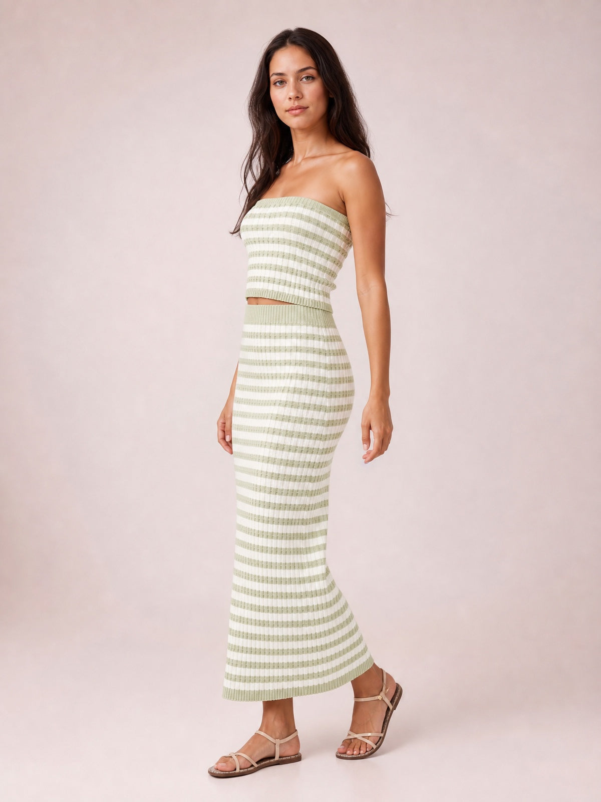 A model poses in a green-and-white striped sweater-style midi dress with a strapless tube top, fitted silhouette, ribbed construction, and flared hem.