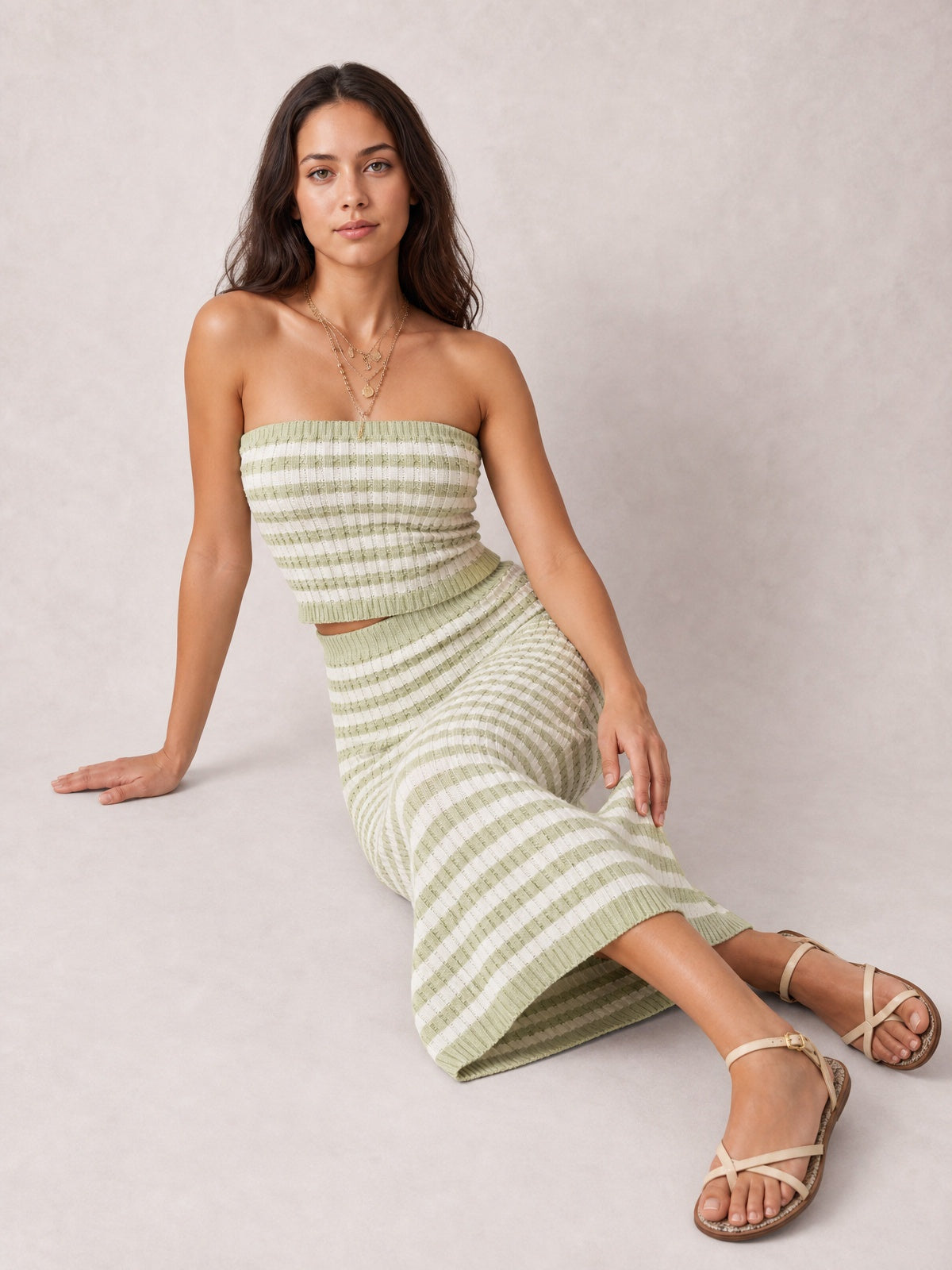 Model seated in a green and white striped sweater-style dress with a strapless tube top, fitted silhouette, and ribbed midi skirt.