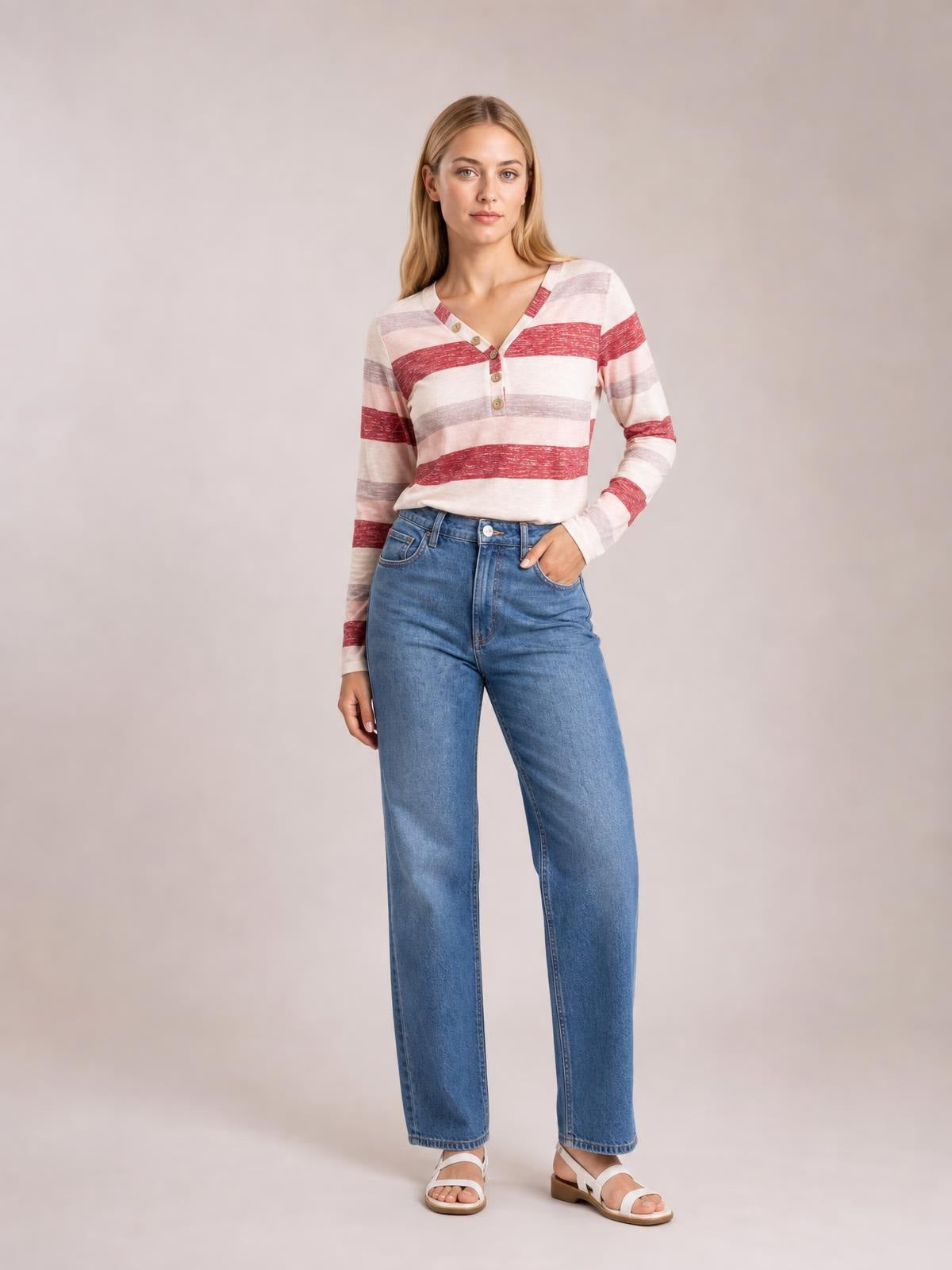 Model wearing a red, pink, and gray contrast striped V-neck long sleeve T-shirt with a buttoned neckline and relaxed silhouette, one hand in her jeans pocket.