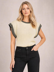 Model poses with one hand in her pocket wearing an ivory ribbed sweater with black contrast trim, cap sleeves, a crew neckline, and a relaxed straight silhouette.