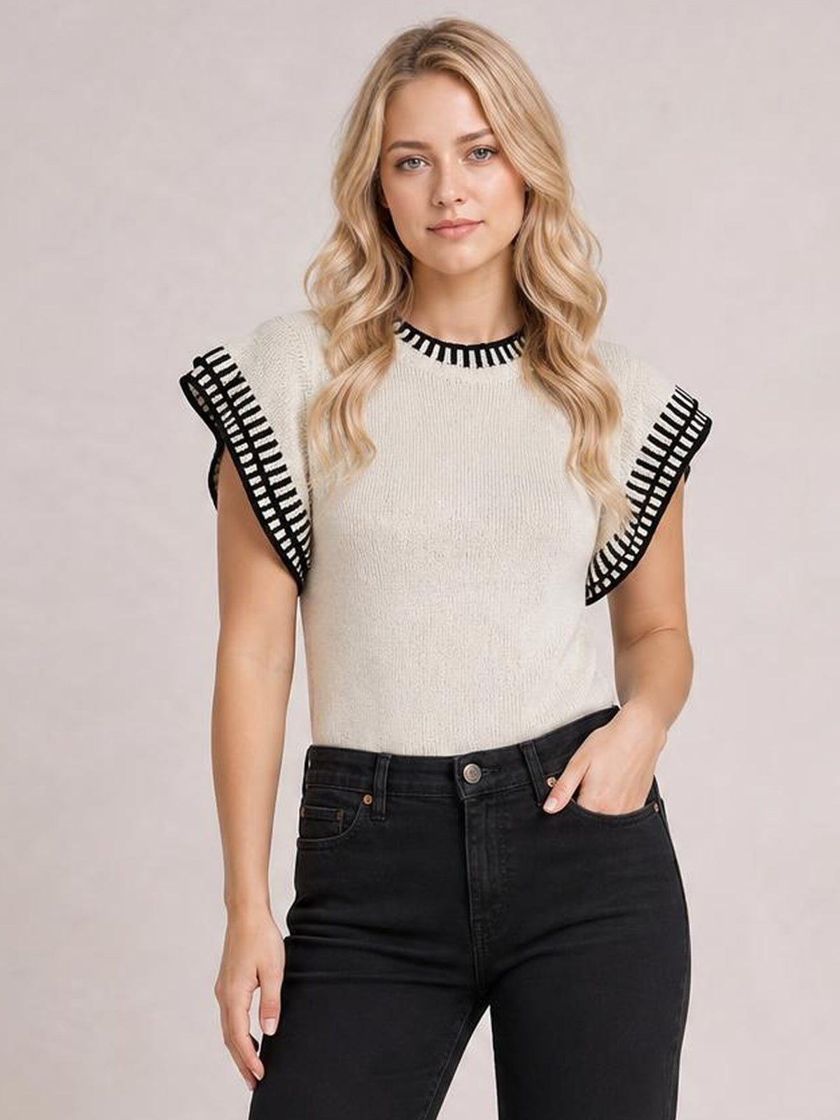 Model wears an ivory ribbed cap-sleeve sweater with bold black contrast trim at the crew neckline and sleeves, shown in a relaxed front-facing pose.