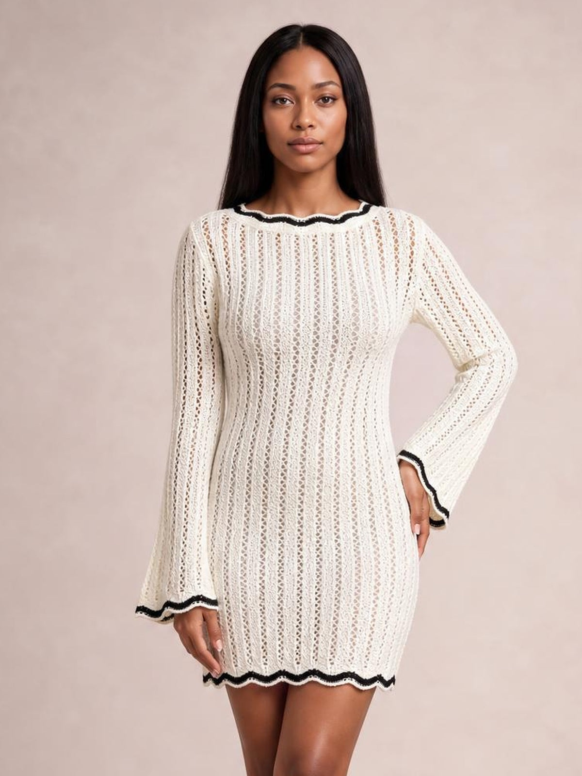 Model wearing an ivory openwork crochet knit sweater dress with black contrast trim, long flared sleeves, a fitted silhouette, and scalloped hem.