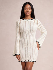Model wearing an ivory openwork crochet knit sweater dress with black contrast trim, long flared sleeves, a fitted silhouette, and scalloped hem.