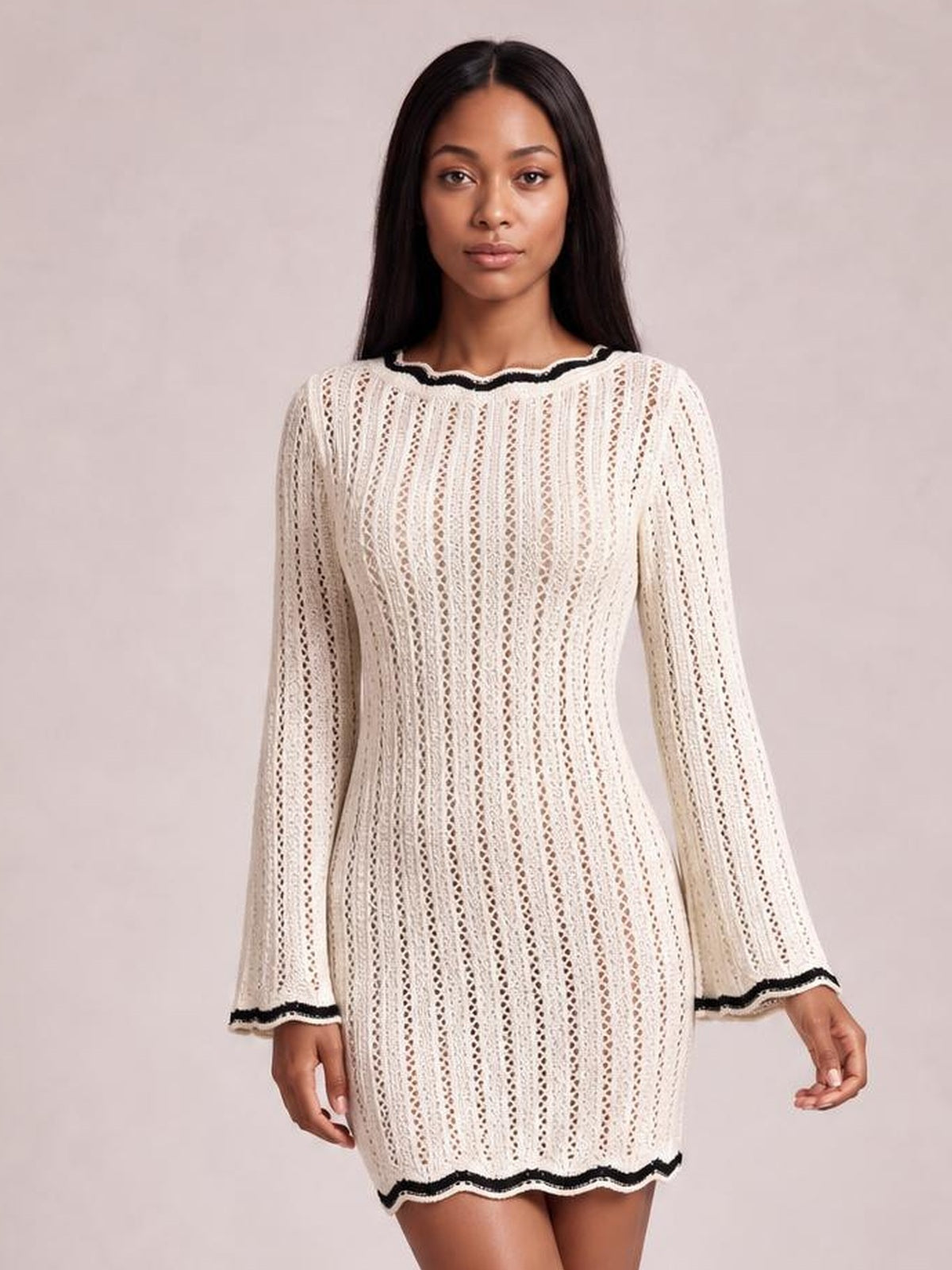 Model wears an ivory crochet knit sweater dress with vertical openwork, long sleeves, a fitted silhouette, and black contrast trim at the neckline, cuffs, and hem.