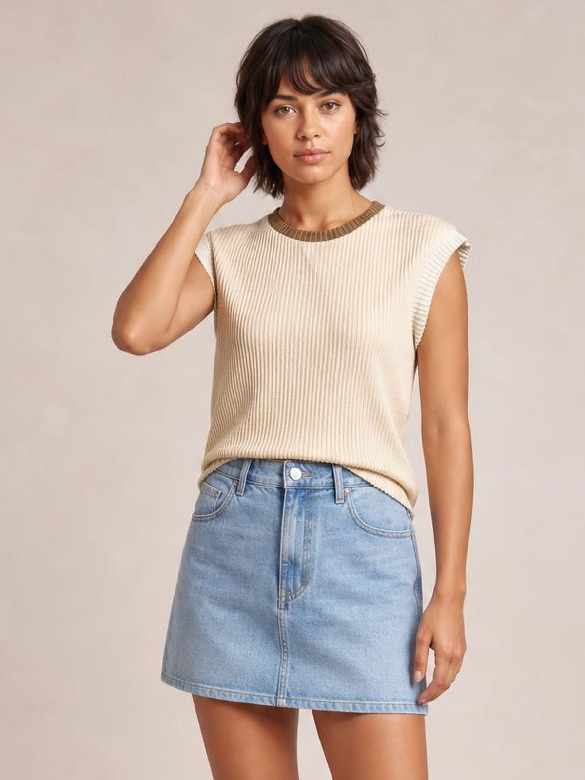 Model poses in a cream ribbed knit sleeveless top with brown contrast trim at the crew neckline and armholes, featuring a straight, slightly relaxed silhouette.