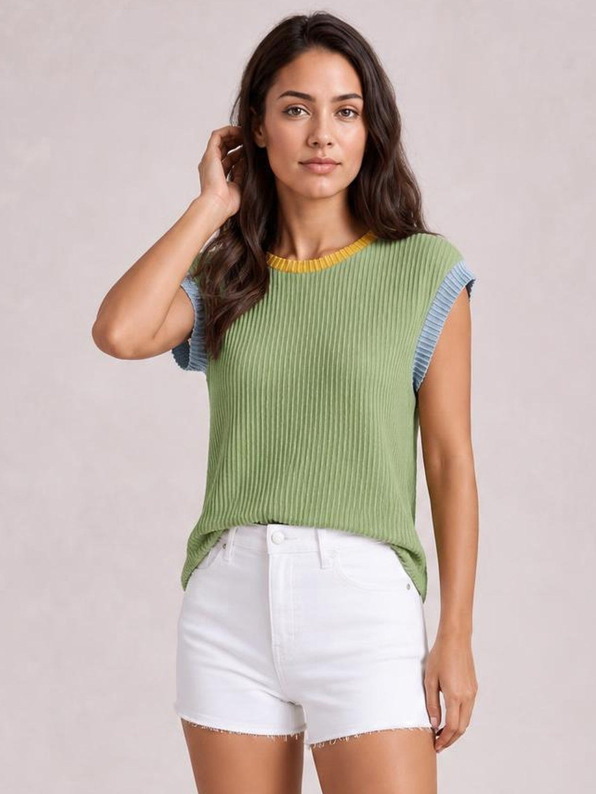 A model poses with one hand in her hair wearing a sage green ribbed knit sleeveless top with yellow neckline and blue contrast trim.