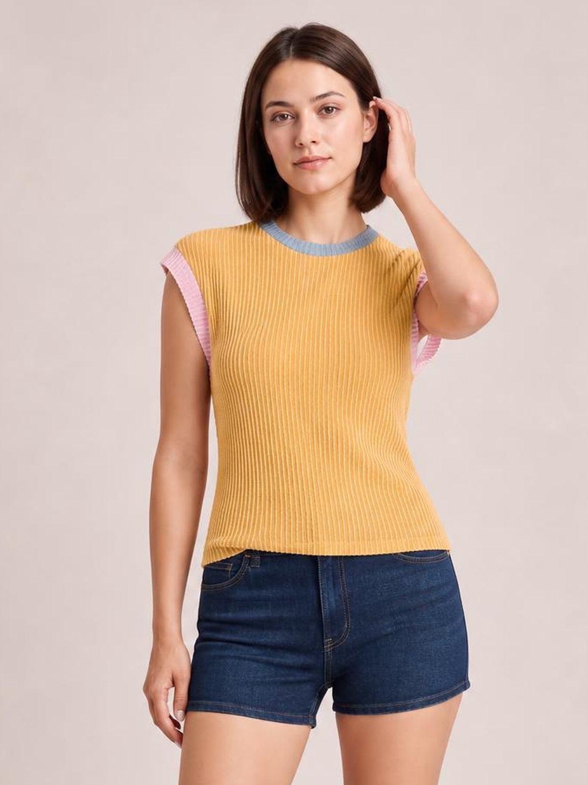 Model poses in a yellow ribbed knit sleeveless top with pink and blue contrast trim, a fitted silhouette, and a slightly curved hem.