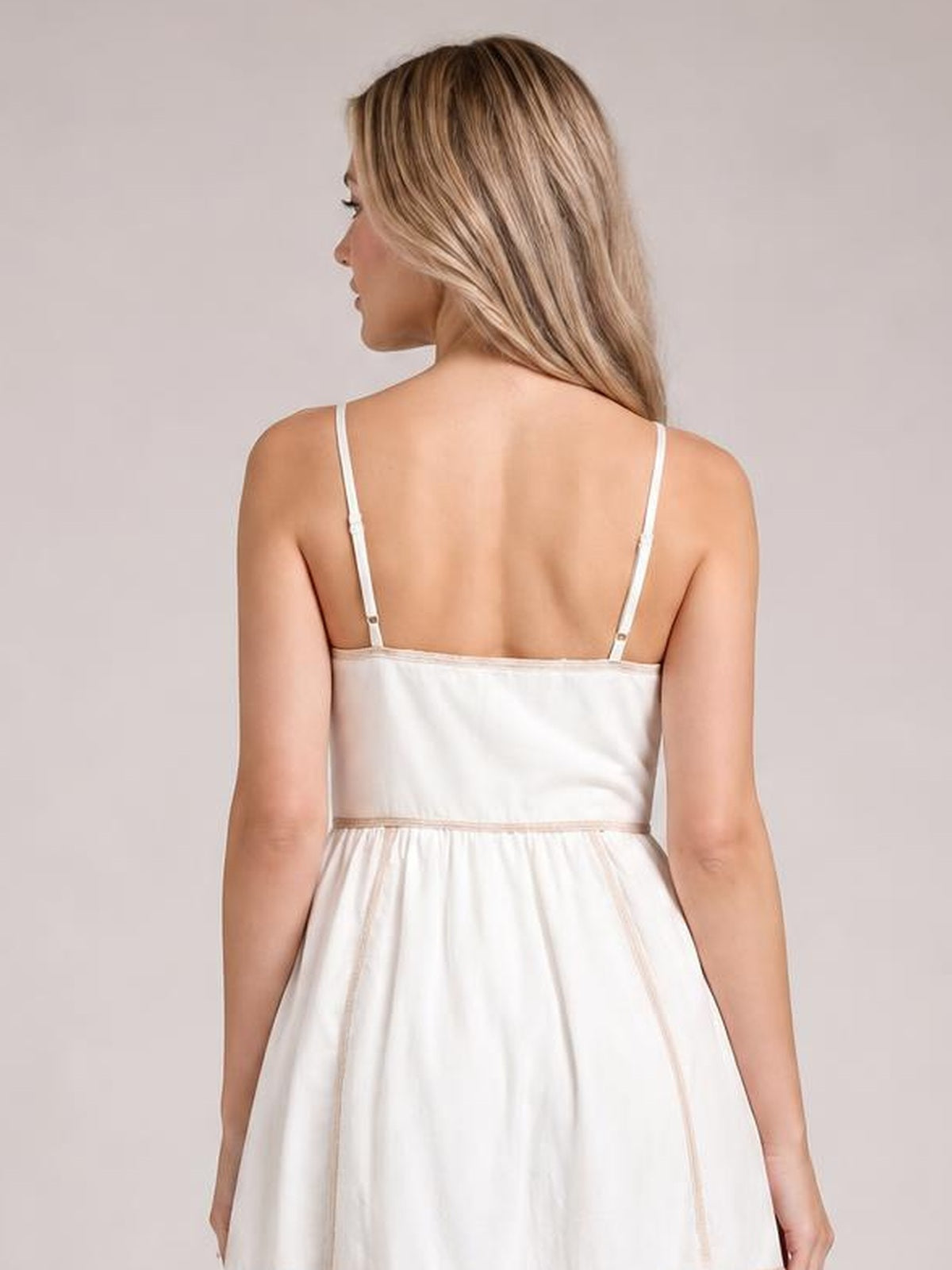 A model shows the back of a white contrast-trim midi cami dress with slender shoulder straps, a fitted bodice, defined waist seam, and softly gathered skirt.