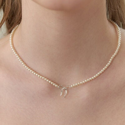 A close-up of a model wearing a delicate synthetic pearl necklace with a petite bow pendant, creating a graceful, feminine silhouette around the neck.