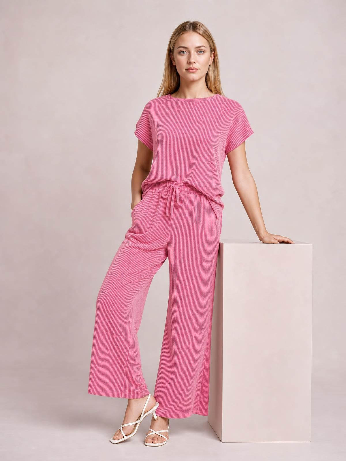 A model poses in a pink corded knit short-sleeve T-shirt and wide-leg pants set with a relaxed silhouette and drawstring waist.