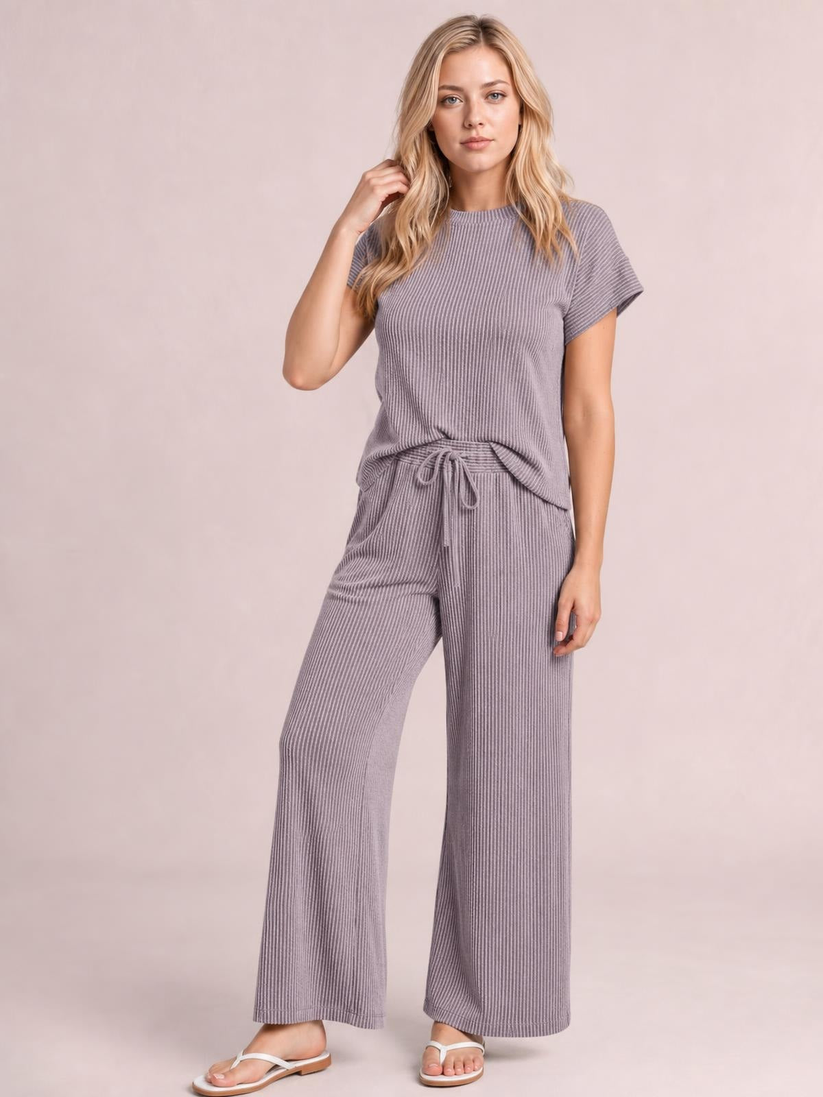 Model wearing a gray corded knit short-sleeve T-shirt and wide-leg pants set, posed with one hand touching her hair and a drawstring waist.