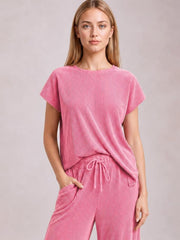 Model poses with one hand in the pocket of a pink corded knit set featuring a short-sleeve T-shirt and wide-leg pants with a drawstring waist.