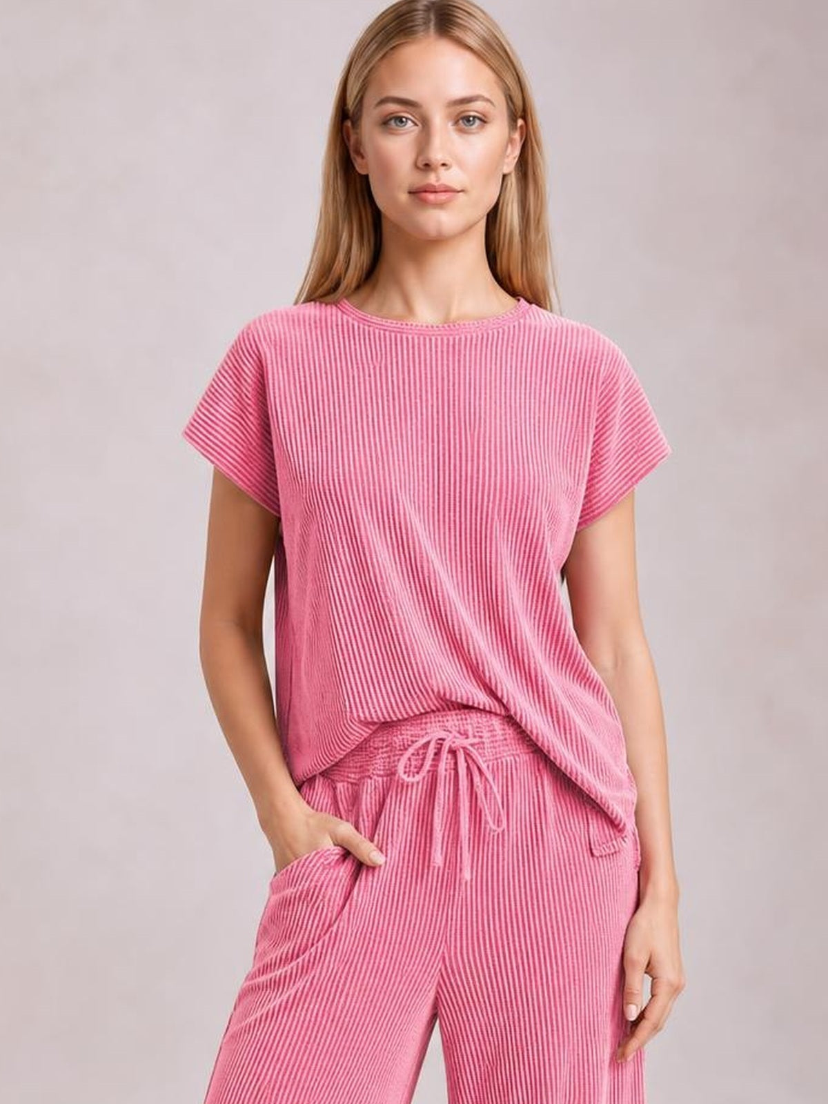 Model poses with one hand in the pocket of a pink corded knit set featuring a short-sleeve T-shirt and wide-leg pants with a drawstring waist.