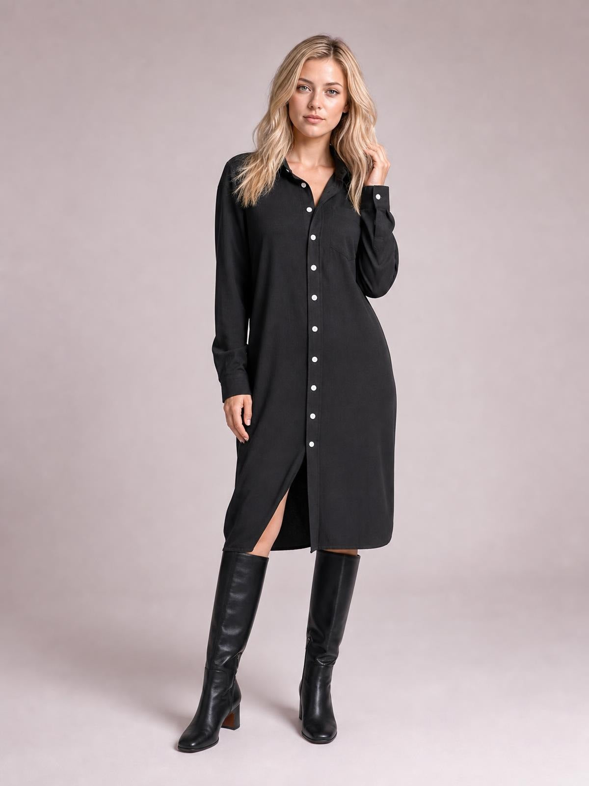 A model poses in a black corduroy shirt dress with a collared button-down front, long sleeves, chest pocket, straight midi silhouette, and front slit.