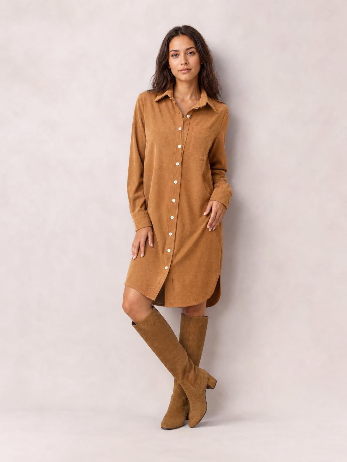 Model poses in a camel corduroy shirt dress with a button-down front, collared neckline, chest pocket, long sleeves, and relaxed straight silhouette.
